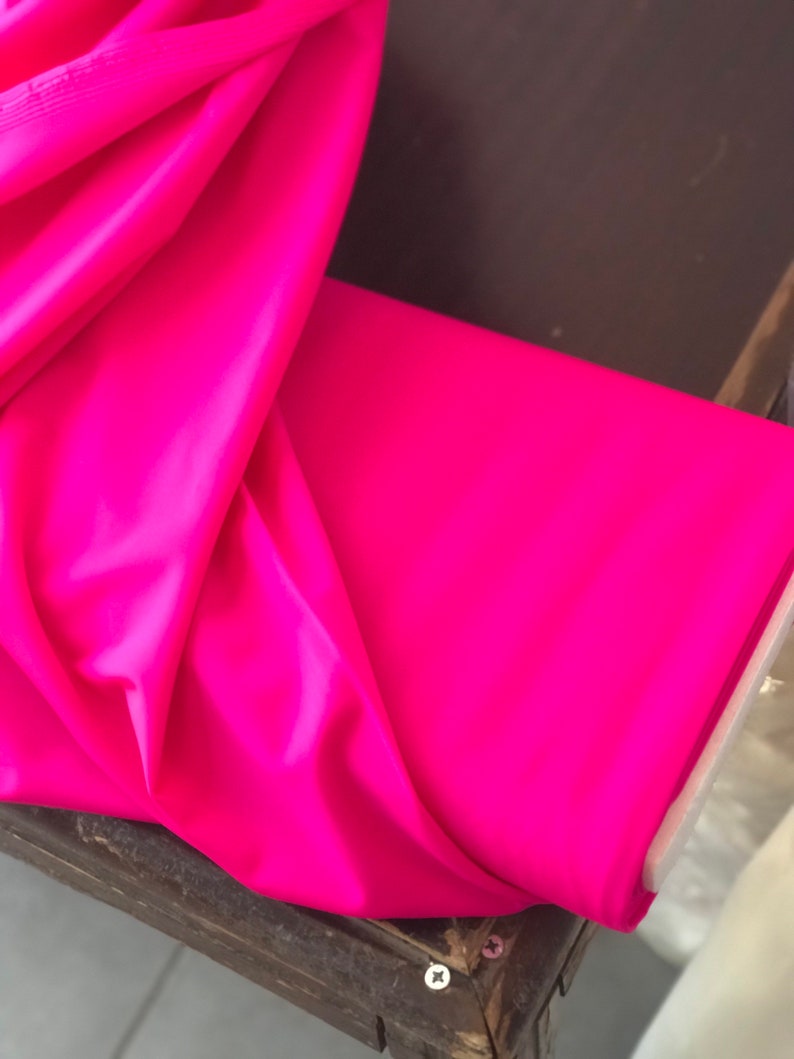 May include: A bright pink fabric folded on a wooden surface. The fabric is smooth and has a slight sheen.