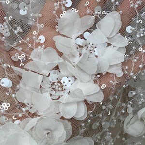Peut inclure: Tissu de dentelle florale blanche avec des paillettes et des perles. Le tissu pr&eacute;sente une base en maille d&eacute;licate avec des applications de fleurs 3D.