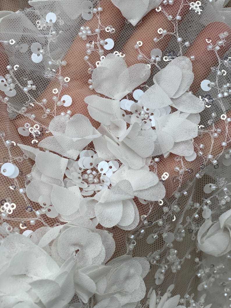 Peut inclure: Tissu de dentelle florale blanche avec des paillettes et des perles. Le tissu pr&eacute;sente une base en maille d&eacute;licate avec des applications de fleurs 3D.