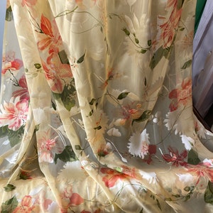 May include: Sheer, light yellow fabric with a floral print of pink and orange flowers. The fabric is draped and has a soft, flowing texture.
