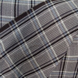 Op de afbeelding: Een close-up van een bruin en wit geruite stof met een diagonaal patroon. De stof is geweven met een herringbone-textuur.