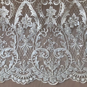 May include: White floral lace fabric with a delicate pattern of flowers and leaves. The lace has a scalloped edge and is perfect for adding a touch of elegance to any project.