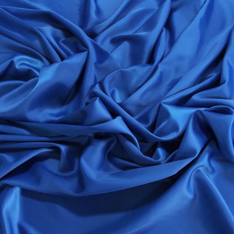 Peut inclure: Gros plan sur un tissu lisse et soyeux de couleur bleu vif. Le tissu est drap&eacute; et pli&eacute;, cr&eacute;ant des lignes et des courbes douces et fluides.