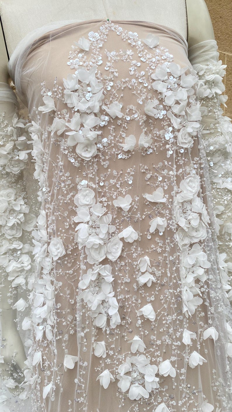 Peut inclure: Tissu de dentelle florale blanche avec des fleurs 3D et des paillettes. Le tissu est transparent et d&eacute;licat, avec une sensation douce et romantique.