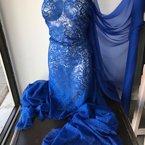 May include: Royal blue lace fabric with a floral pattern. The lace has a frayed edge and is displayed on a mannequin.