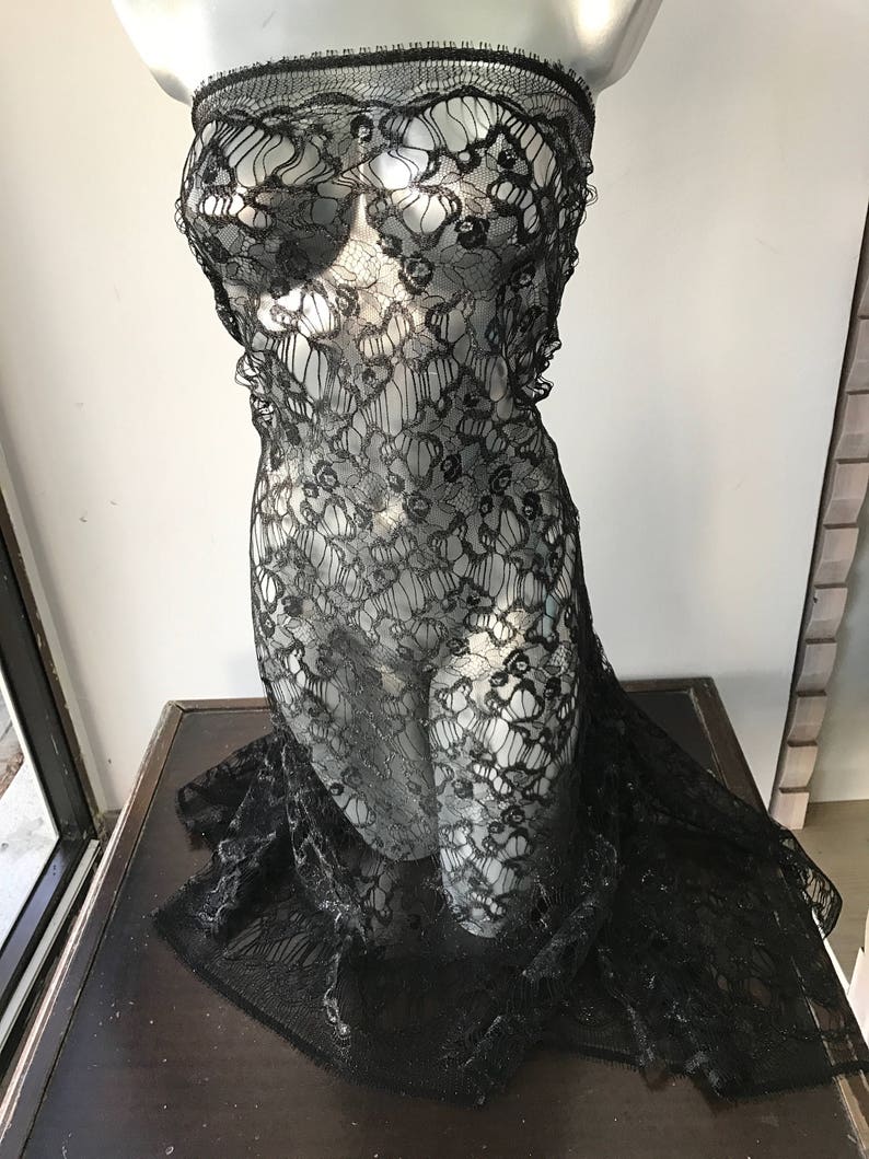 May include: Black lace fabric with a delicate floral pattern. The fabric is sheer and has a soft, flowing texture.