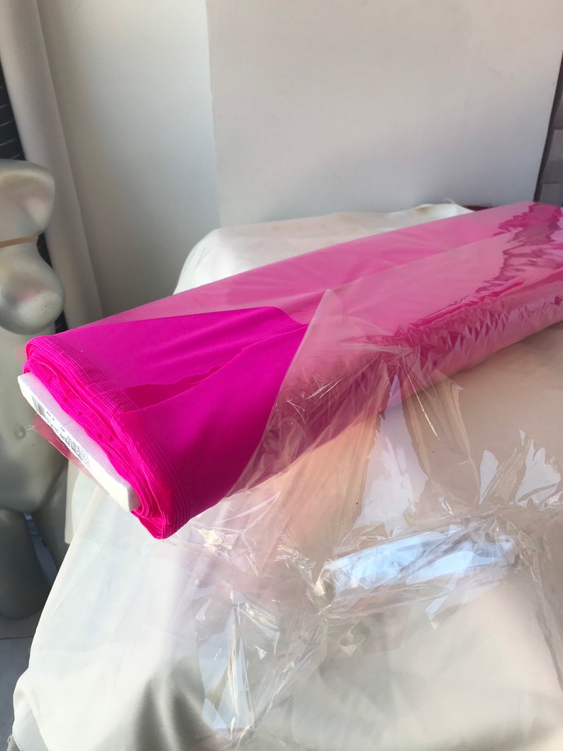 May include: A roll of bright pink fabric wrapped in clear plastic. The fabric is folded neatly and appears to be a lightweight material.