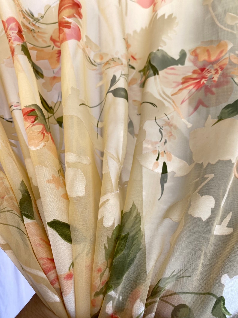 May include: A sheer curtain panel with a floral pattern in shades of pink, white, and green. The fabric is lightweight and translucent, creating a soft and airy feel.