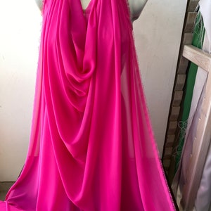 Op de afbeelding: Een helder roze, doorschijnende stof met een rafelige rand. De stof is gedrapeerd over een mannequin.