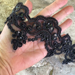 May include: Black lace trim with black sequins and beads. The trim has a scalloped edge.