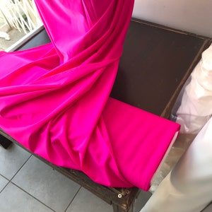May include: A bright pink fabric draped over a wooden table. The fabric is smooth and has a slight sheen.