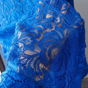 May include: Close-up of a blue lace fabric with a floral pattern. The lace is delicate and intricate, with a soft, flowing texture.