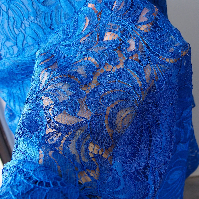 May include: Close-up of a blue lace fabric with a floral pattern. The lace is delicate and intricate, with a soft, flowing texture.