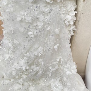 Peut inclure: Tissu de tulle blanc avec des embellissements floraux 3D blancs et des paillettes argent&eacute;es.