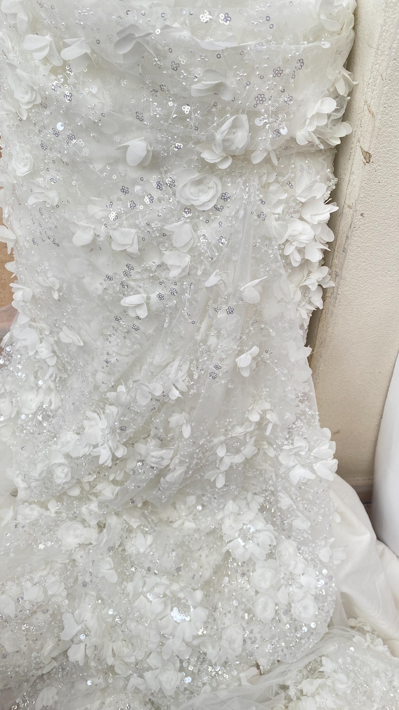 Peut inclure: Tissu de tulle blanc avec des embellissements floraux 3D blancs et des paillettes argent&eacute;es.