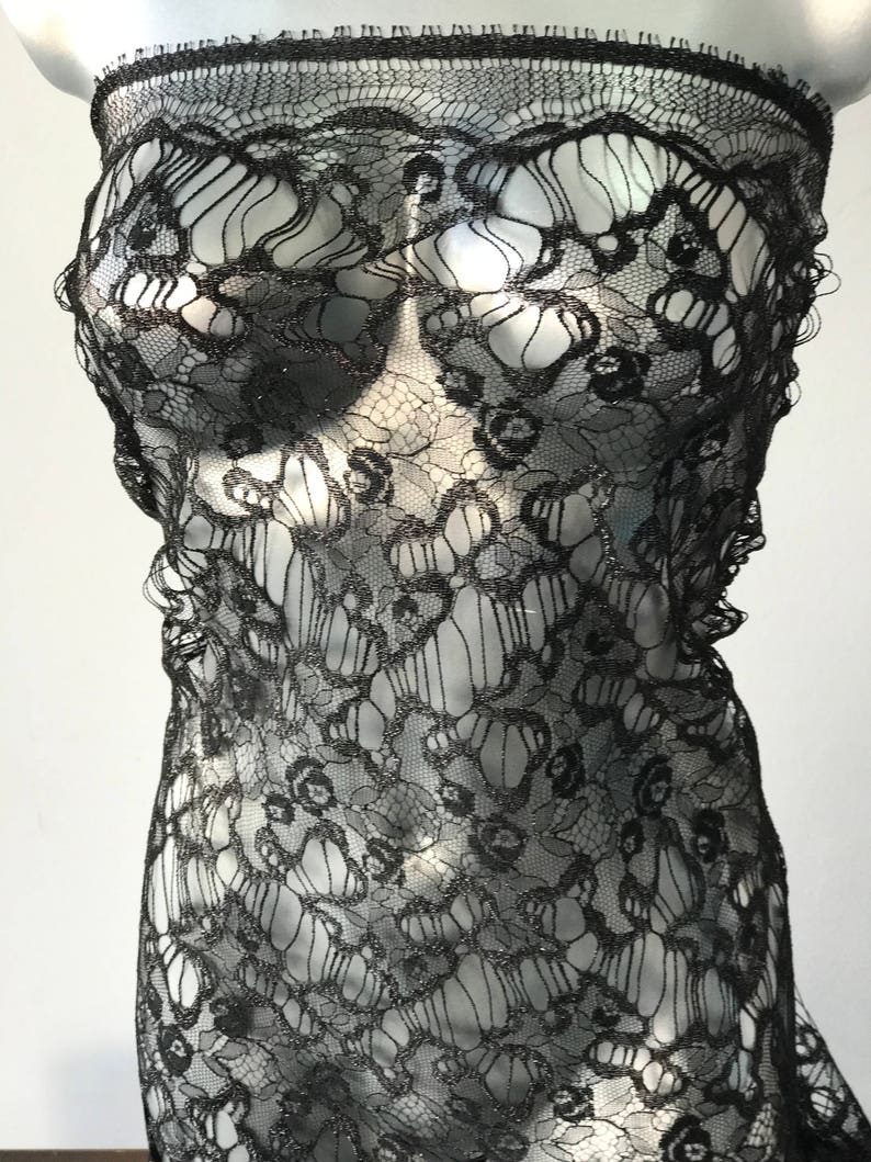 May include: Black lace fabric with a delicate floral pattern. The lace has a shimmery finish.