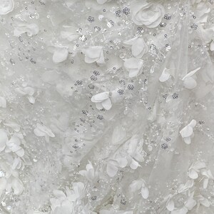 Peut inclure: Tissu blanc avec un motif floral d&eacute;licat et des paillettes argent&eacute;es. Le tissu est transparent et a une sensation douce et romantique.
