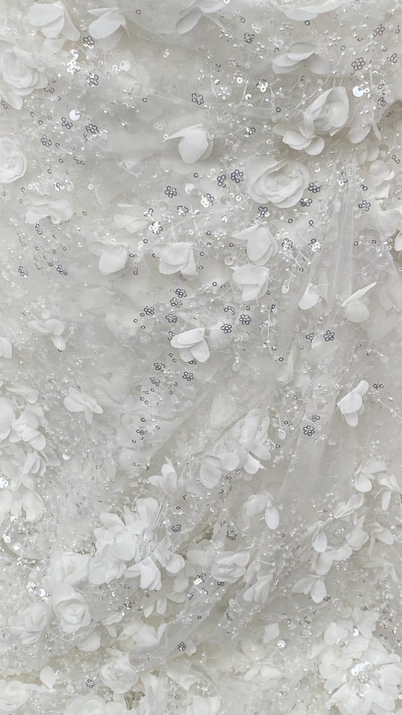 Peut inclure: Tissu blanc avec un motif floral d&eacute;licat et des paillettes argent&eacute;es. Le tissu est transparent et a une sensation douce et romantique.