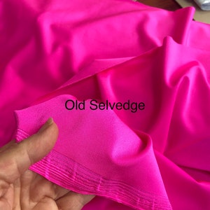 May include: Close-up of a bright pink fabric with a folded edge. The edge is a selvedge, which is a finished edge of woven fabric. The text "Old Selvedge" is written on the fabric.