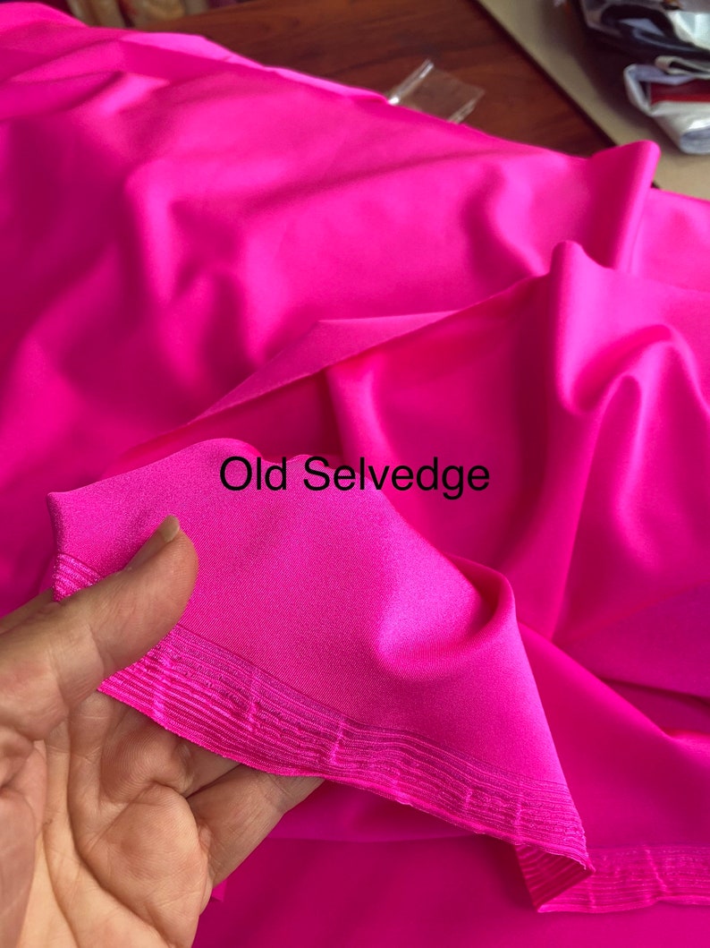 May include: Close-up of a bright pink fabric with a folded edge. The edge is a selvedge, which is a finished edge of woven fabric. The text "Old Selvedge" is written on the fabric.
