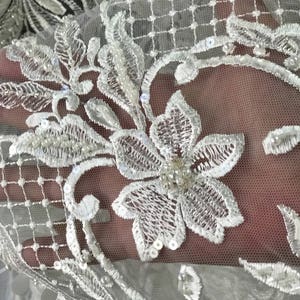 May include: White lace fabric with a floral pattern and pearl embellishments. The lace is delicate and intricate, with a soft, flowing texture.
