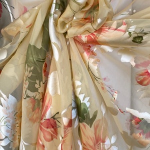 May include: A sheer, light yellow scarf with a floral print. The flowers are in shades of pink, green, and white.