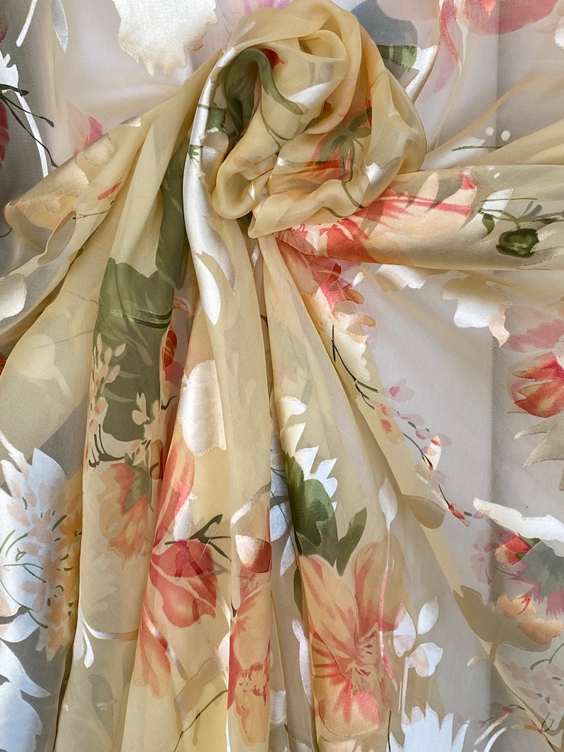 May include: A sheer, light yellow scarf with a floral print. The flowers are in shades of pink, green, and white.