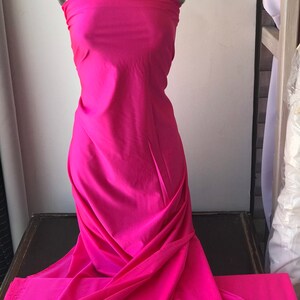 May include: A bright pink fabric swatch draped over a mannequin. The fabric is smooth and has a slight sheen.
