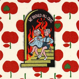 Peut inclure: Un patch brodé noir et jaune avec deux figures de diables rouges assises sur un escalier devant une porte enflammée. Le texte "WE SHOULD ALL QUIT" est écrit en arc au-dessus de la porte.