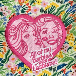 Könnte beinhalten: Rosa gestickter Herz-Patch mit zwei weiblichen Figuren und dem Text "All of my Barbies were Lesbians!"