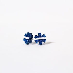 May include: A pair of blue glitter stud earrings with a white star of life design.