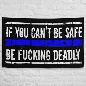 May include: Black flag with white text that reads "IF YOU CAN'T BE SAFE BE FUCKING DEADLY." A blue line is centered horizontally. The flag has grommets in the corners for hanging.