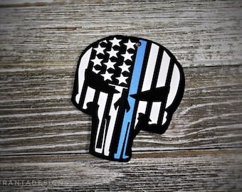 May include: A black and white skull silhouette with an American flag design and a thin blue line down the center. The skull is on a wood background.