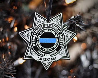 May include: A black and white star-shaped ornament with the text "Department of Public Safety, Great Seal of the State of Arizona, State Trooper, Arizona" and a blue and black thin blue line ribbon.