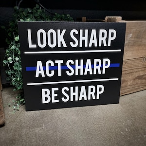 May include: Black sign with white text that reads "Look Sharp", "Act Sharp", and "Be Sharp". A thin blue line is above the word "Act".