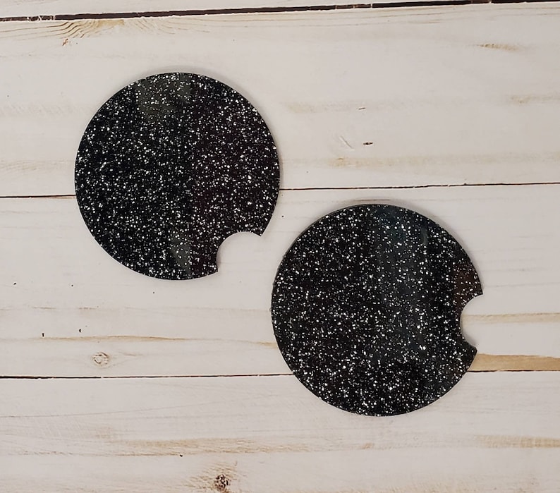 Pu&ograve; includere: Due sottobicchieri rotondi neri con una finitura glitterata bianca. I sottobicchieri hanno un'apertura per una tazza.