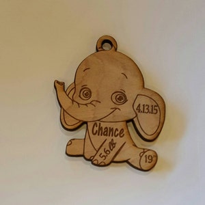 May include: Wooden elephant ornament with the name "Chance" and the date "4.13.15" engraved on it. The ornament also includes the measurements "5.6 lbs" and "19" inches.