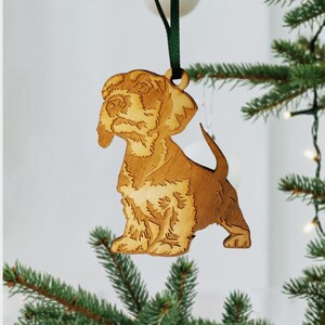 May include: A wooden Christmas ornament shaped like a brown and white dog. The ornament is hanging from a green ribbon.