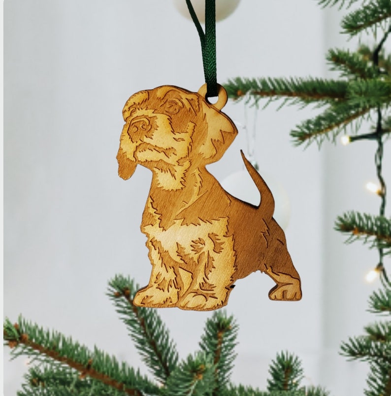 May include: A wooden Christmas ornament shaped like a brown and white dog. The ornament is hanging from a green ribbon.