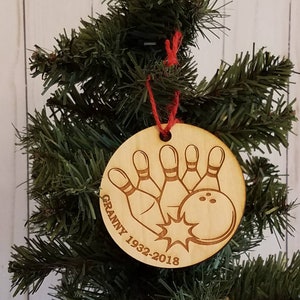 May include: A wooden Christmas ornament with a bowling ball and pins design. The ornament is engraved with the text "Granny 1932-2018".