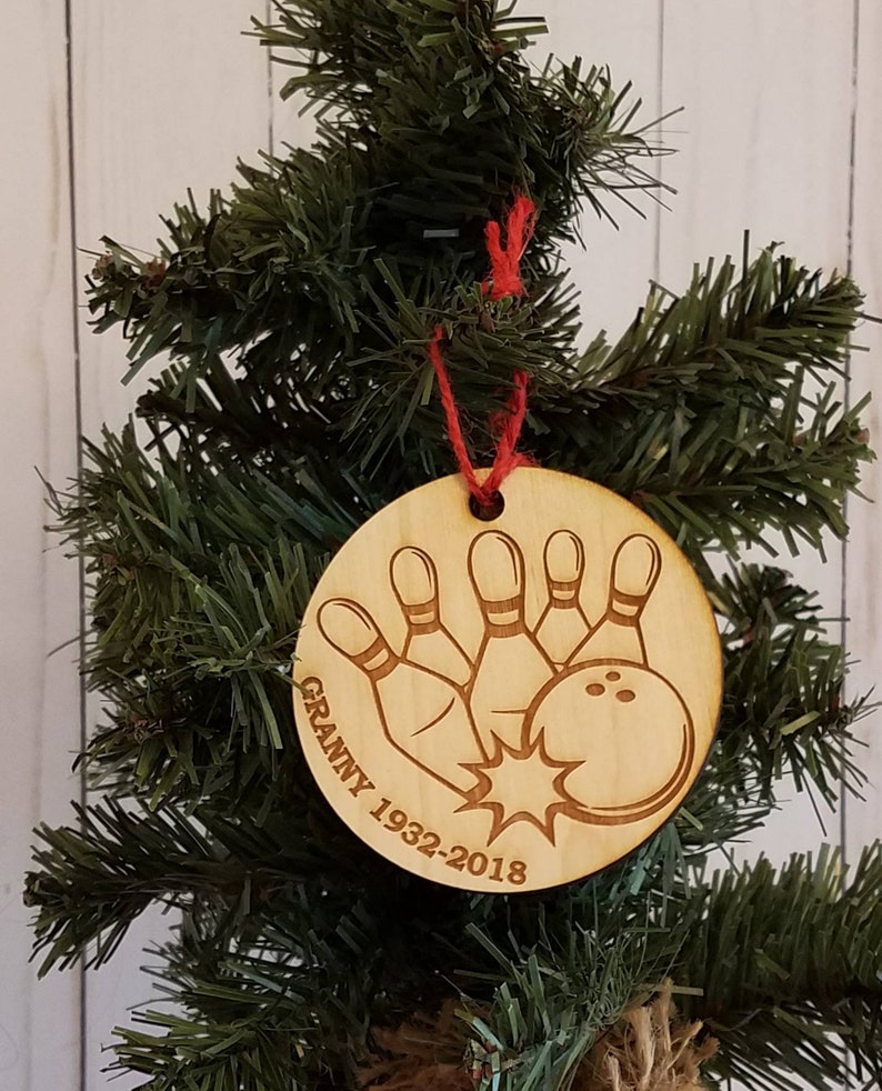 May include: A wooden Christmas ornament with a bowling ball and pins design. The ornament is engraved with the text "Granny 1932-2018".
