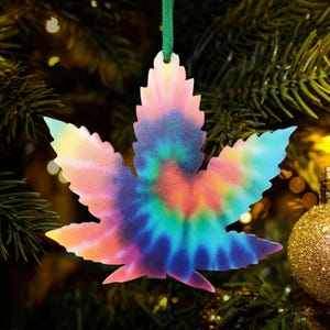 May include: A tie-dye cannabis leaf Christmas ornament. The ornament is a light pink, blue, green, and orange color.