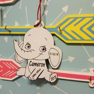 May include: A white wooden elephant ornament with black details. The ornament is personalized with the name "Cameron", the date "10/22/18", the weight "7lbs 16oz", and the length "20.5" inches.