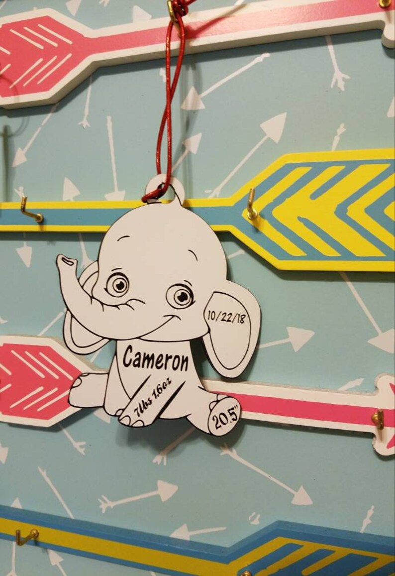 May include: A white wooden elephant ornament with black details. The ornament is personalized with the name "Cameron", the date "10/22/18", the weight "7lbs 16oz", and the length "20.5" inches.