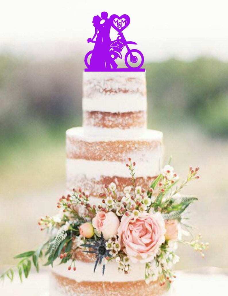 May include: Purple wedding cake topper featuring a bride and groom riding a motorcycle with a heart that says "M&M".