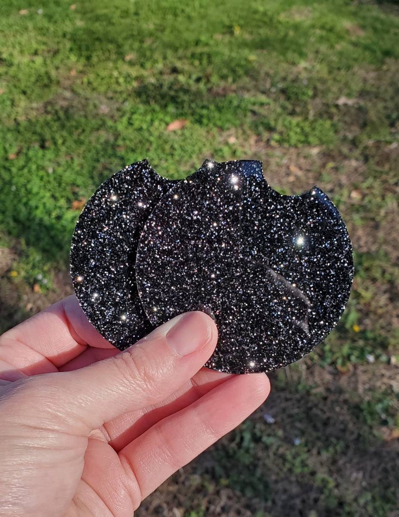 Pu&ograve; includere: Due sottobicchieri rotondi di glitter nero. I sottobicchieri hanno la forma di un cerchio con un bordo leggermente irregolare. I sottobicchieri sono fatti di un materiale di glitter nero.