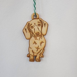 May include: A wooden ornament of a dachshund dog with a green and white string for hanging.