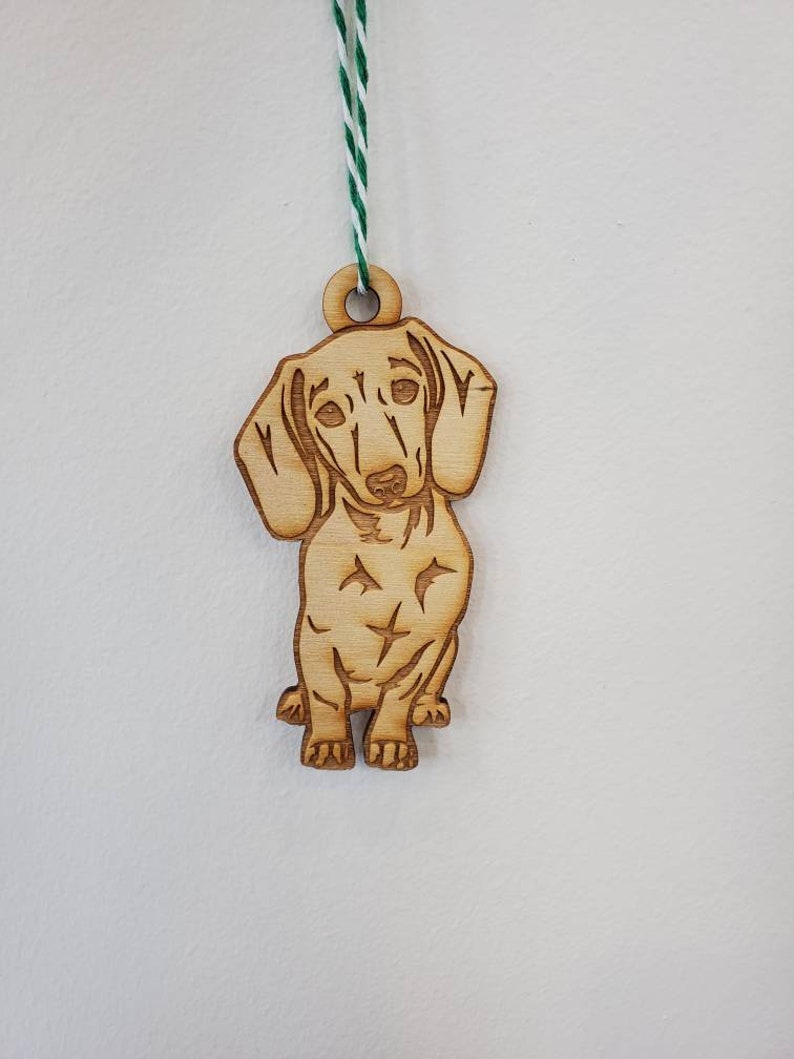 May include: A wooden ornament of a dachshund dog with a green and white string for hanging.