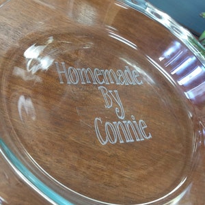 May include: A clear glass pie plate with a scalloped edge. The plate is engraved with the text "Homemade by Connie".