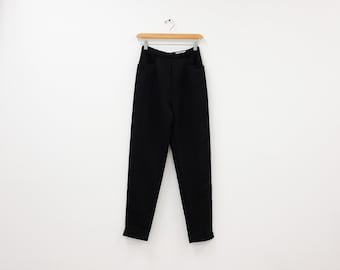 Könnte beinhalten: Schwarze Hose, die an einem Holzbügel an einer weißen Wand hängt.